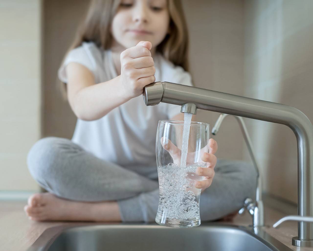 A little girl saving water by using a modern faucet to care for the environment