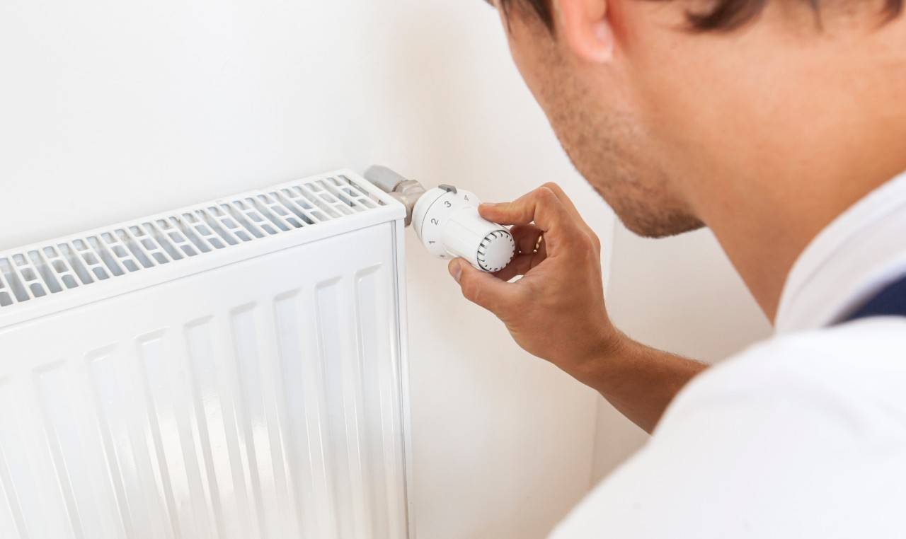 a man adjusting the temperature on a radiator with a smart thermostat