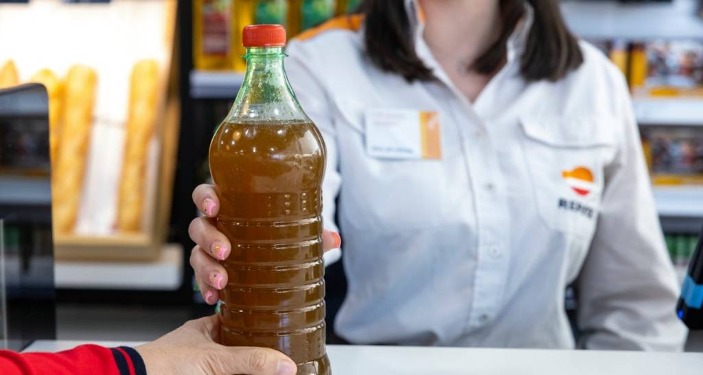 A bottle with used cooking oil being handed to a Repsol service station staff member