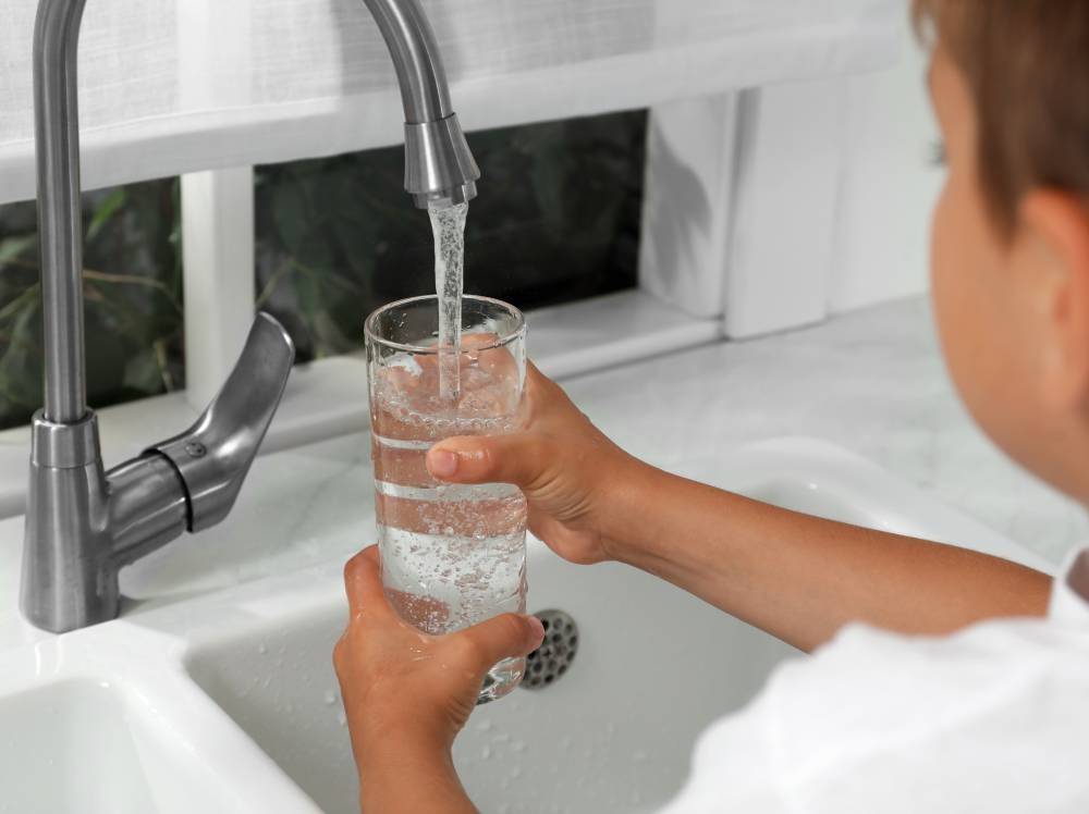 A child filling up a glass with water from a faucet